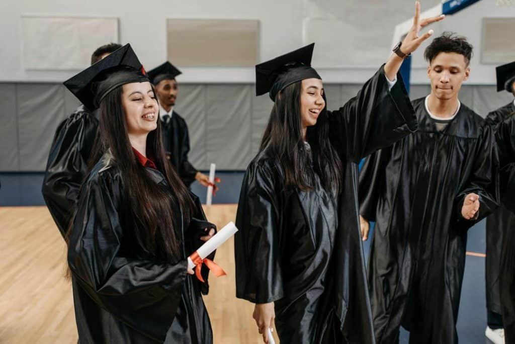 Group of diverse graduates in black gowns celebrating after receiving diplomas.