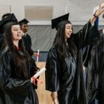 Group of diverse graduates in black gowns celebrating after receiving diplomas.