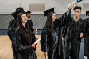 Group of diverse graduates in black gowns celebrating after receiving diplomas.