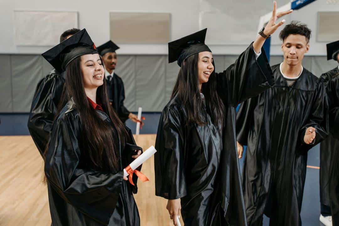 Group of diverse graduates in black gowns celebrating after receiving diplomas.