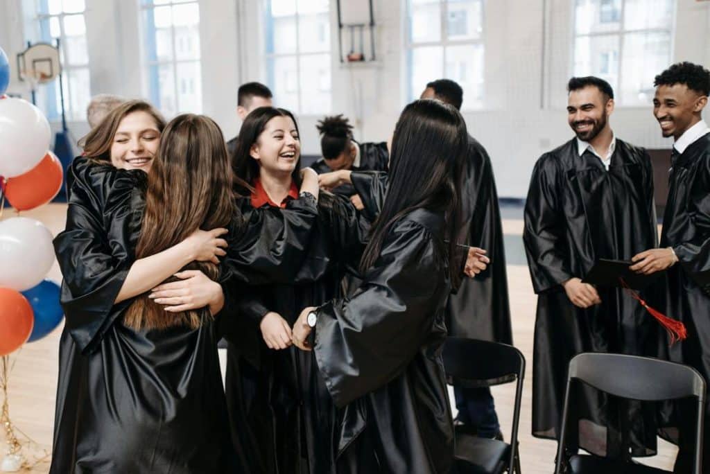 Group of diverse graduates in black gowns celebrating after receiving diplomas.
