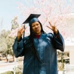 Student in graduation cap and gown raising hands outdoors