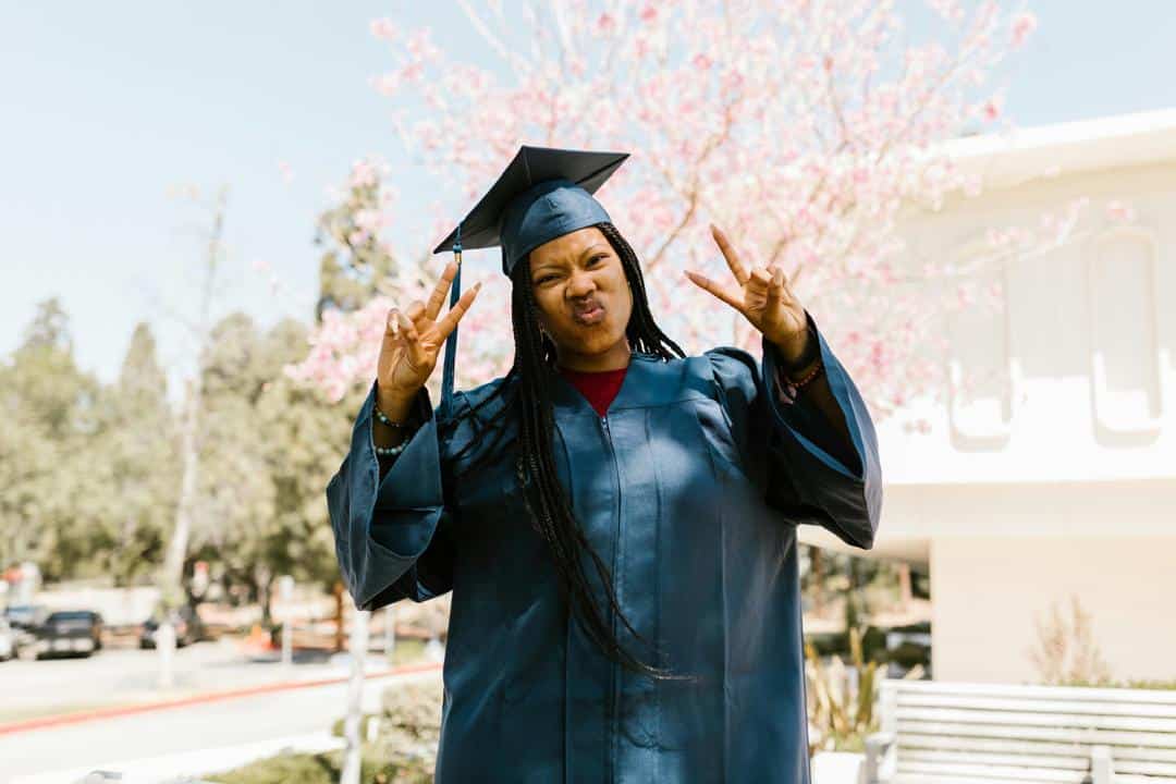 Student in graduation cap and gown raising hands outdoors